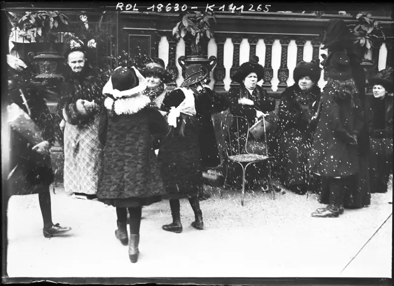 Photographie de 1912 : sur un trottoir parisien, des passants en manteaux d'hiver se lancent des confettis