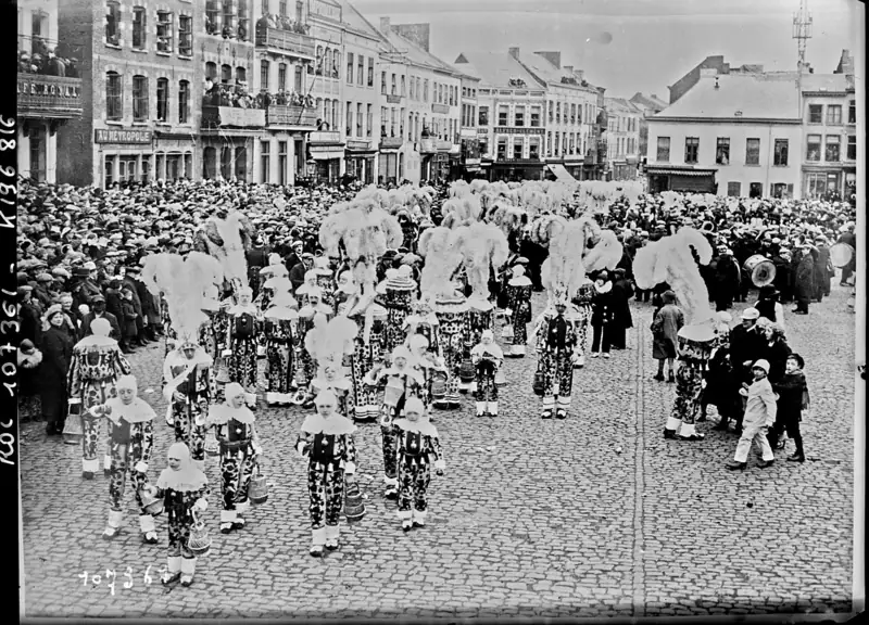 Photographie de 1926 : des dizaines de Gilles en costume et grands chapeaux de plumes d'autruche défilent sur la Grand-Place de Binche devant une foule immense