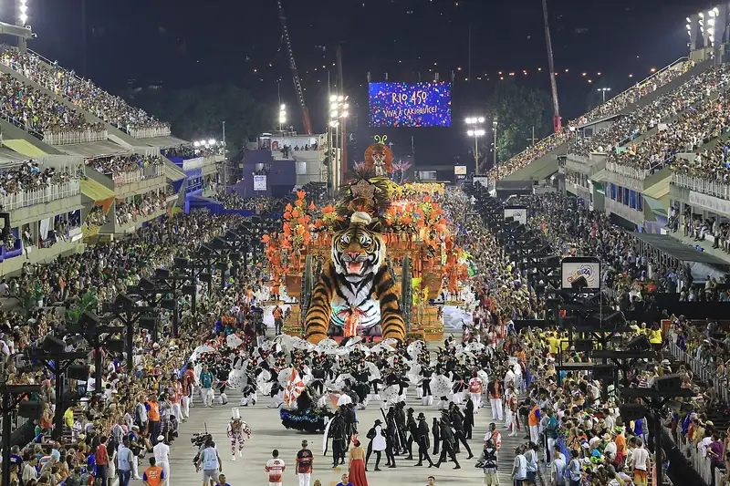 Vue plongeante de nuit sur le Sambódromo : un char géant en forme de tigre avance entre des gradins noirs de monde