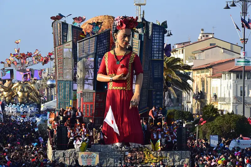 Char géant : une grande femme en robe rouge et fleurs dans les cheveux, devant des immeubles colorés, au-dessus de la foule