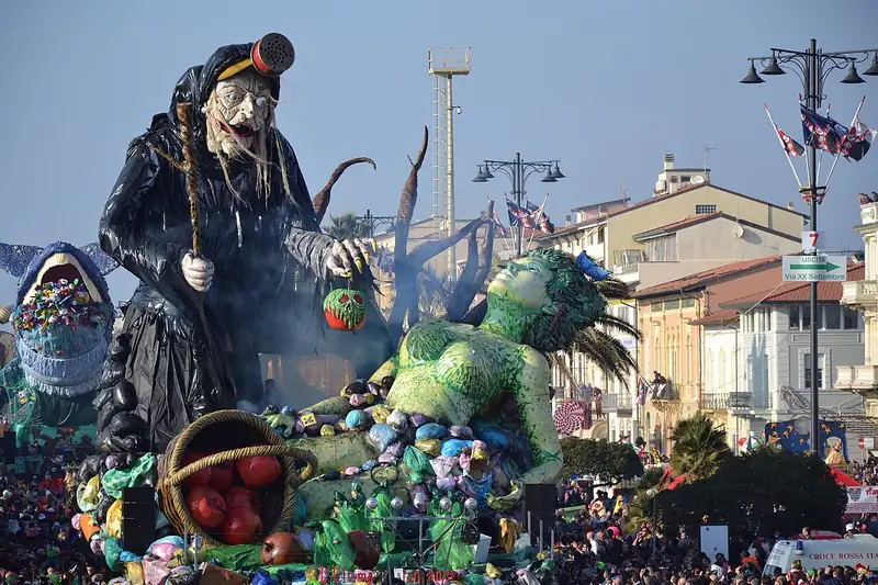 Char géant sur le front de mer de Viareggio : une sorcière noire tenant une pomme, entourée d'un dragon vert et de fruits, devant une foule immense