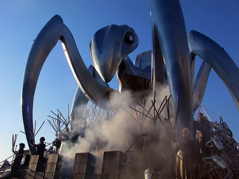 Une araignée métallique géante aux longues pattes argentées, dans un nuage de fumée
