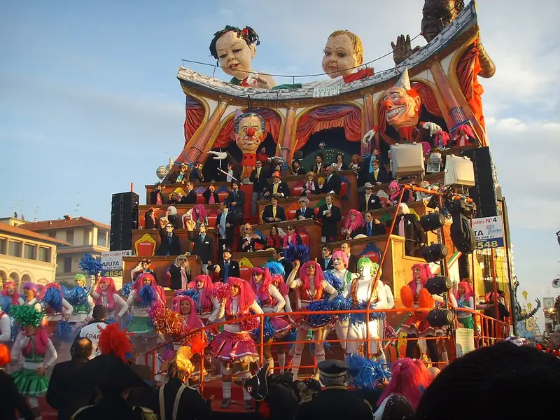Char géant en forme d'hémicycle parlementaire : des personnages en costume sur les bancs, un clown au nez rouge au centre, des têtes géantes au sommet et des pom-pom girls au premier plan
