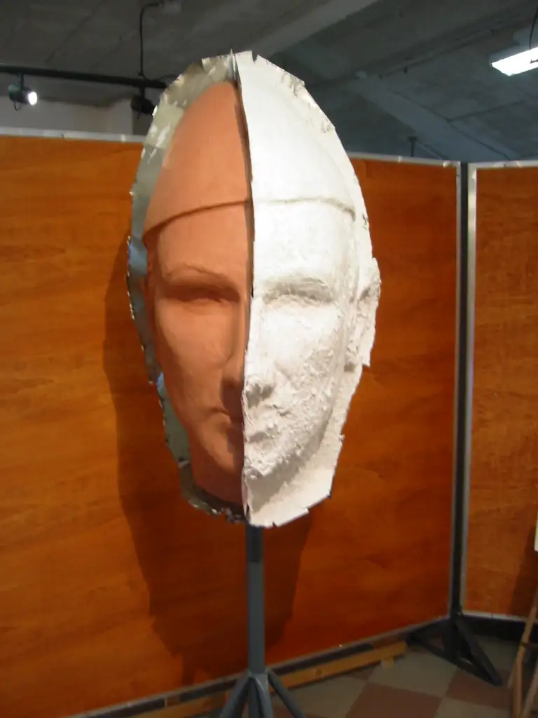 Un visage sculpté, moitié en argile, moitié recouvert de son moule en plâtre blanc